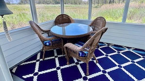 A covered patio with a round table and four wicker chairs, a blue and white patterned floor, and a view of a grassy field and trees. - GREAT LOCATION!  Million dollar view of the Salt Pond  (Bethany Beach)
