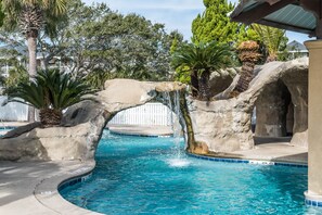 Una piscina con caída de agua, rodeada de palmeras y rocas.