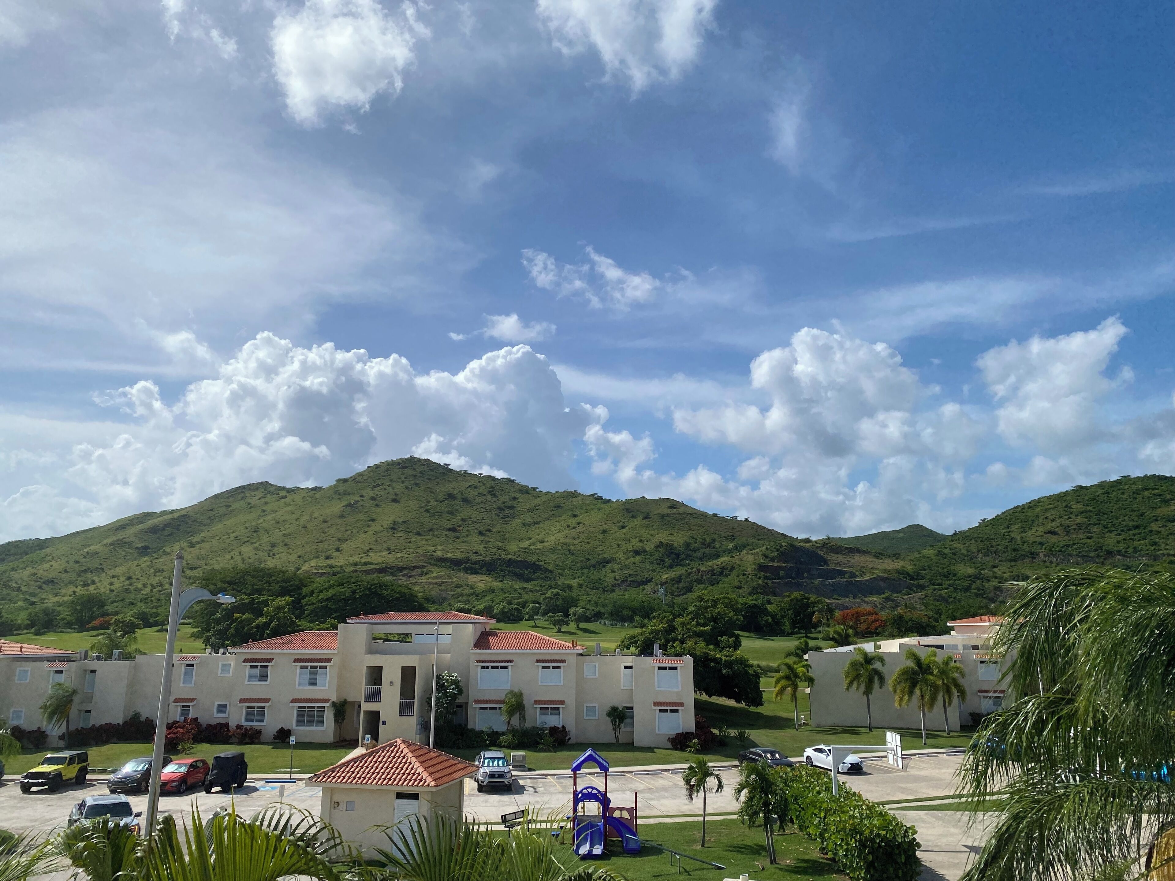 A hotel with a parking lot, a playground, and a view of green hills.