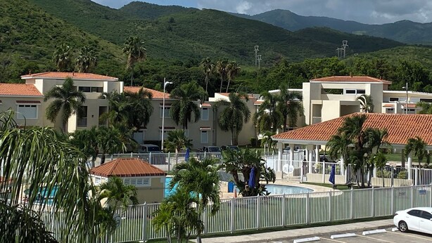 Un resort con varias edificaciones, piscina y montañas al fondo.