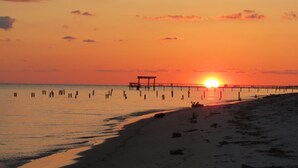 Una spiaggia con un molo che si protende verso il mare al tramonto.