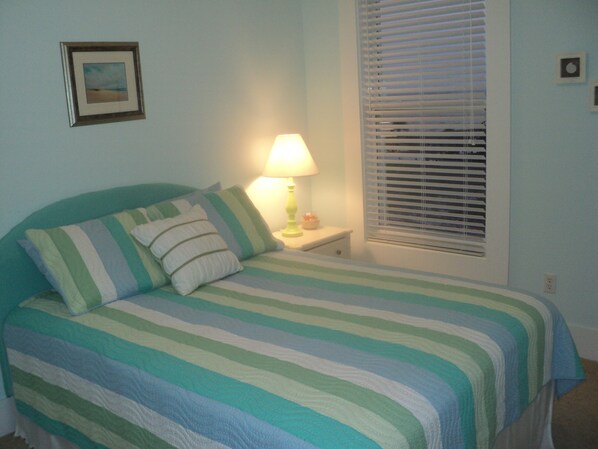 A bedroom with a bed, pillows, a nightstand, a lamp, a window with blinds, and a framed picture on the wall. - 'Seaglass'-Perfect Beach House with Pool, Peaceful and Private (Ocean Springs)