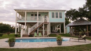 Una casa a due piani con un portico coperto, una piscina e un’area salotto esterna.