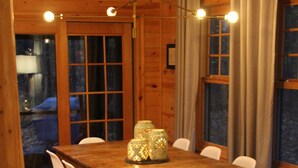 Una mesa de madera para comer con sillas blancas, una araña y cortinas en las ventanas.