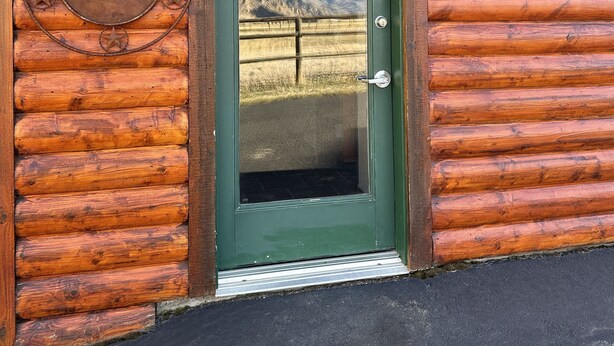 A log cabin with a green door, a welcome sign, and a number plaque. - Looking for an Alternative to a Big Box Motel?  We're it! (Gardiner)
