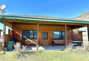 A wooden cabin with a porch, a door, windows, a satellite dish, a trash can, and a bicycle.