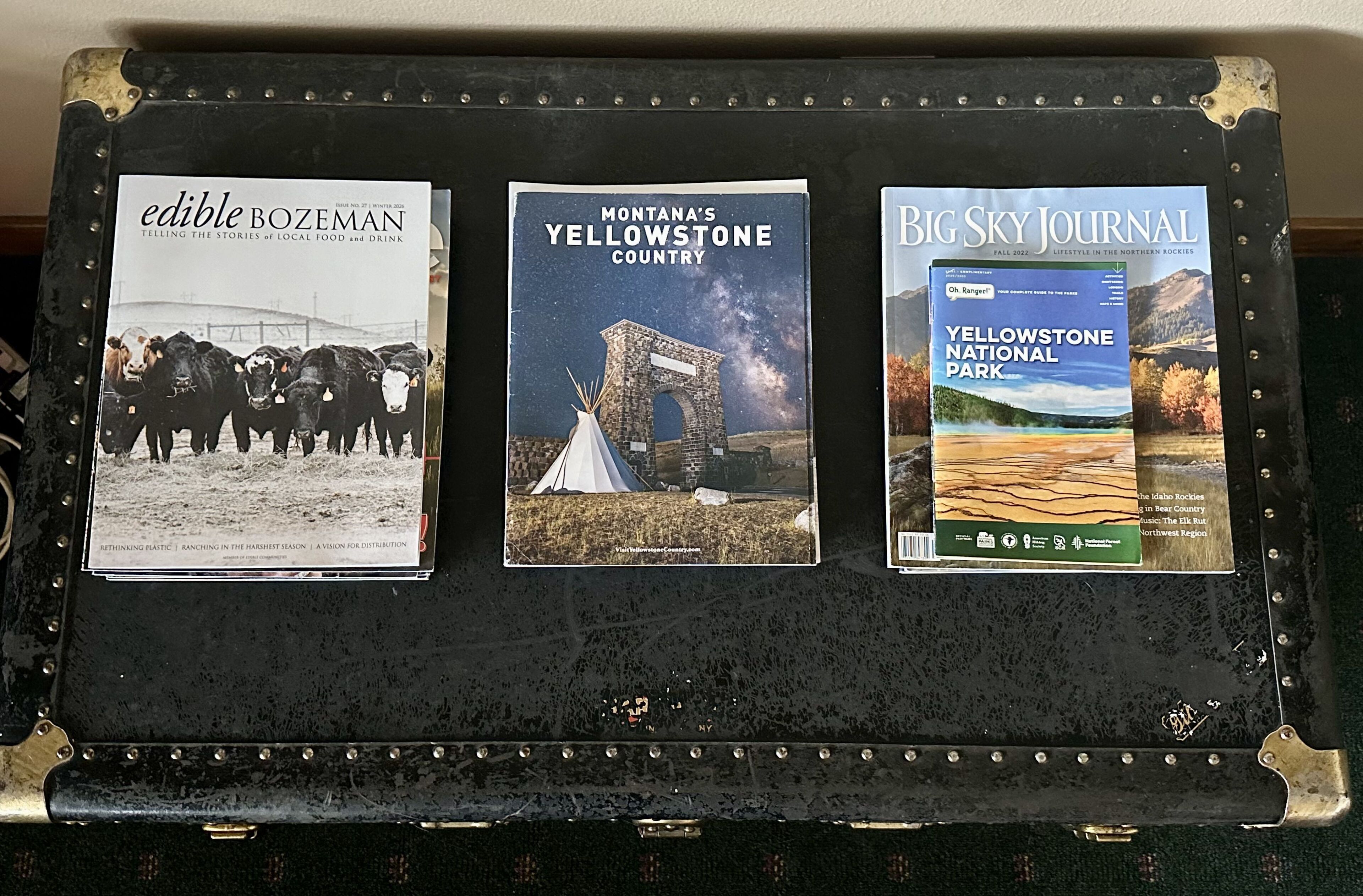 A suitcase with three magazines: 'Edible Bozeman,' 'Montana's Yellowstone Country,' and 'Big Sky Journal.'