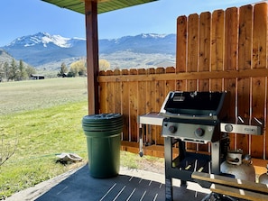 A barbecue grill with a view of mountains, a wooden fence, and a green trash can.