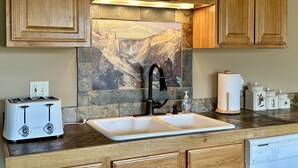 A kitchen with wooden cabinets, a stone backsplash, a sink, a toaster, and a dishwasher. - Looking for an Alternative to a Big Box Motel?  We're it! (Gardiner)