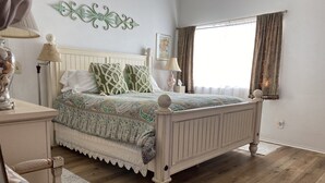 Een slaapkamer met een houten bed, een wit hoofdeinde, een bed met een opvallend sprei en een raam met gordijnen.