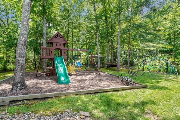 A playground with a swing set, slide, and climbing structure surrounded by trees. - Country Charmer with Inviting Front and Back Porches, Swim Spa, Decks, Fire Pit (Canton)