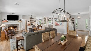 Een ruime woonkamer met een open haard, een eethoek met een houten tafel, en een keuken op de achtergrond.
