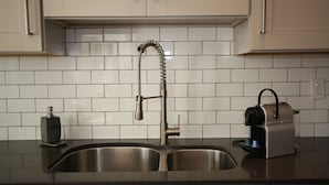 A kitchen with a stainless steel sink, a built-in espresso machine, and white tiled backsplash.