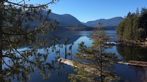 A calm lake with mountains in the background, surrounded by trees and a wooden dock.
