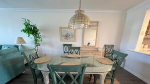 Comedor con una mesa redonda de vidrio, sillas verdes y una lámpara colgante.