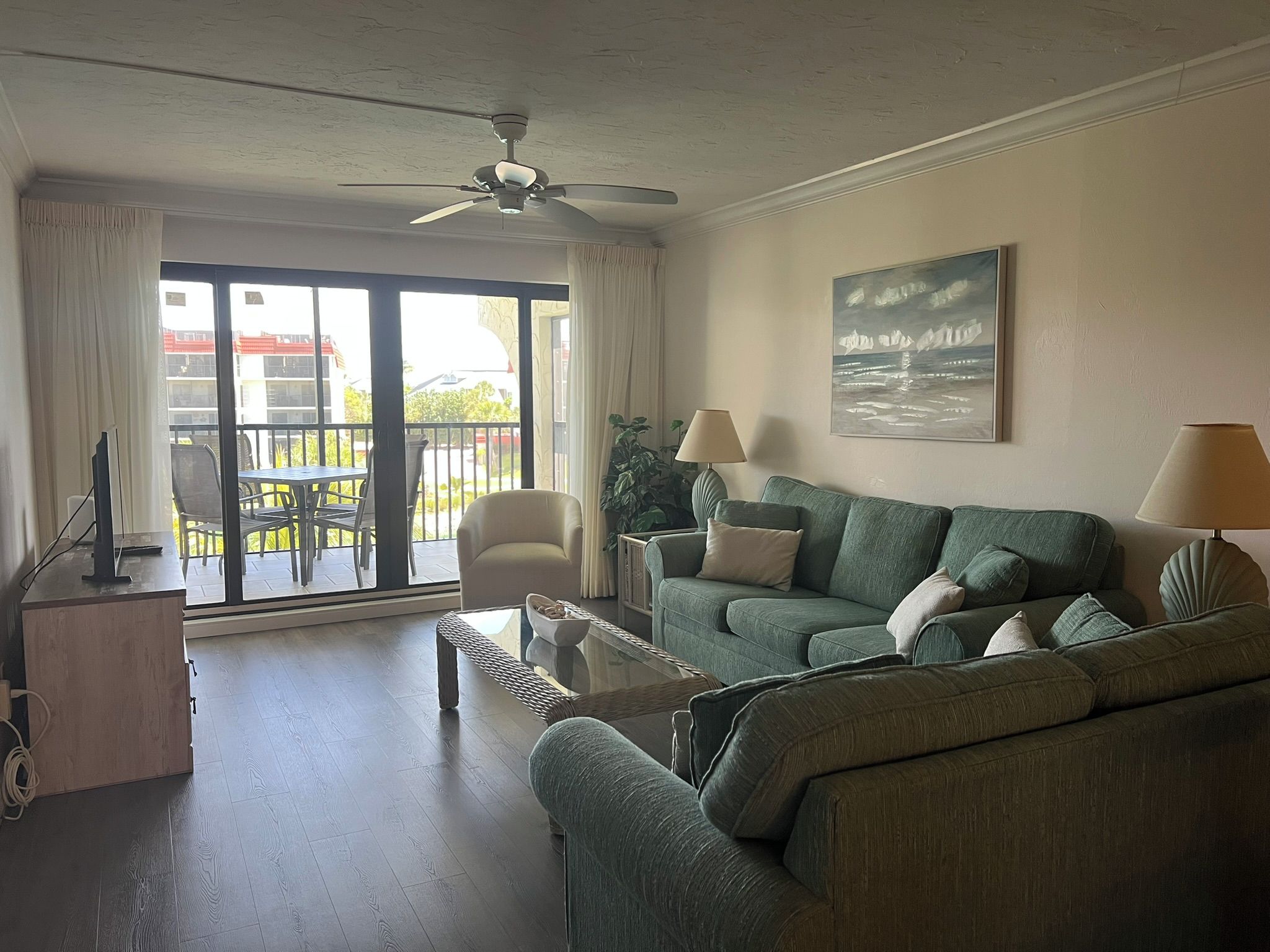 Een woonkamer met een bank, fauteuils, een salontafel, een plafondventilator en uitzicht op een balkon met buitenmeubilair.