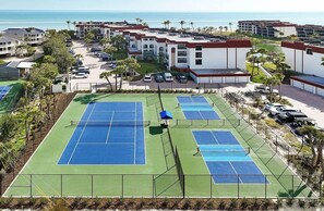 Ein Tennisplatzkomplex mit mehreren Plätzen, umgeben von Gebäuden und Palmen.