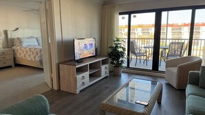 Habitación de hotel con balcón, cama, televisor, mesa de centro y zona de estar.
