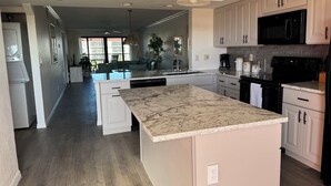 Una cocina moderna con muebles blancos, una isla grande con encimera de mármol y electrodomésticos negros.