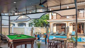 An indoor pool area with a pool table, lounge chairs, and a dining table.