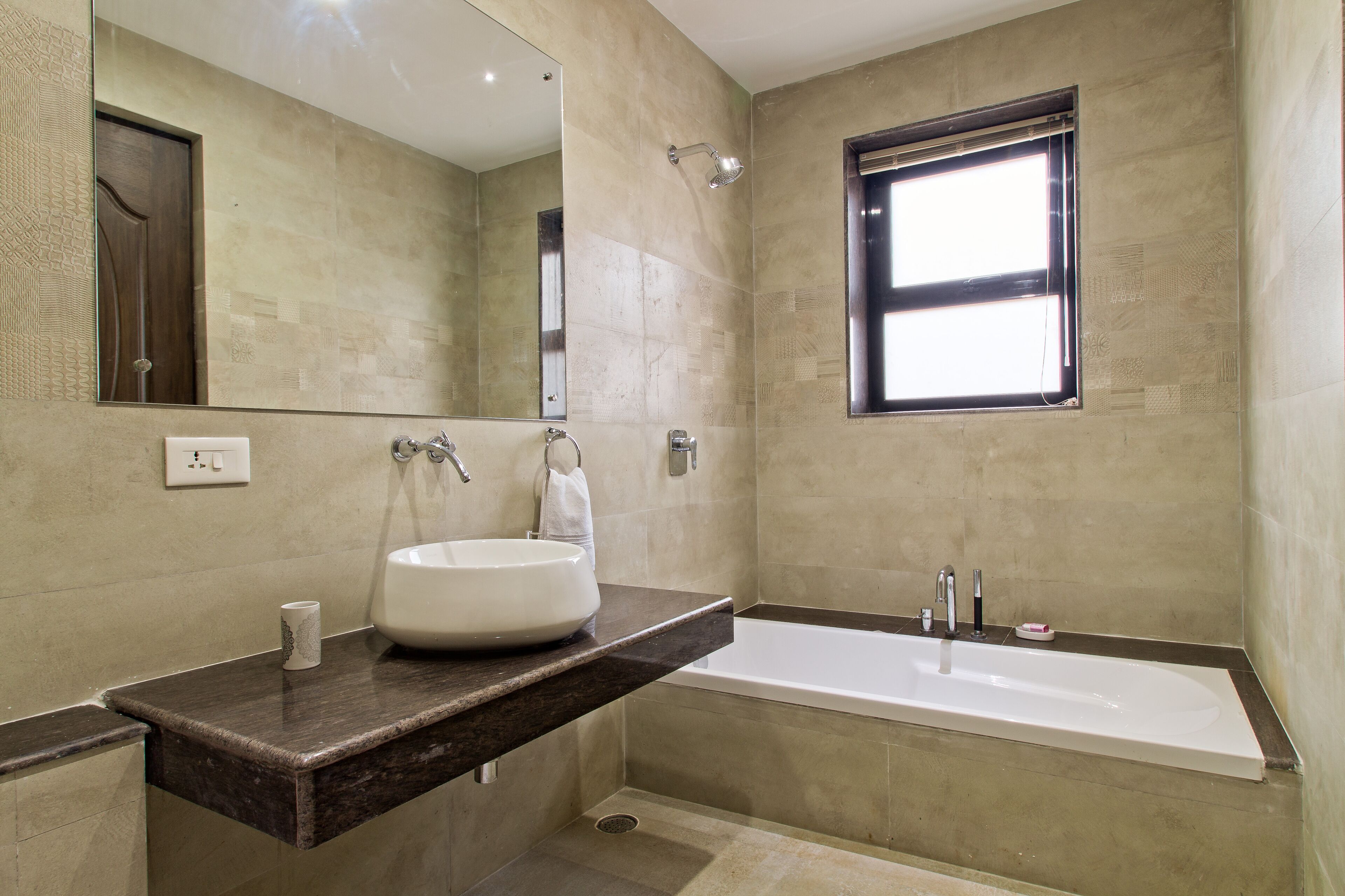 Une salle de bain moderne avec une grande baignoire, un lavabo rond, un miroir et une fenêtre.