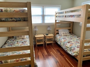 Une chambre avec un lit superposé, une fenêtre, deux tables de chevet et une petite table de nuit.
