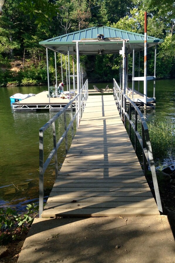 A wooden dock leading to a covered area with a boat docked at the end. - Experience Kentucky Lake out the back door! Spacious 4-bedroom retreat awaits. (Murray)