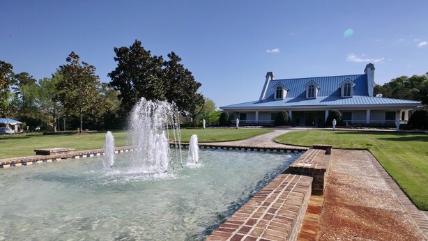 A clear pool with a fountain, surrounded by a brick border, and a building with a blue roof in the background.