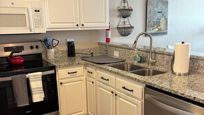 A kitchen with white cabinets, stainless steel appliances, a granite countertop, a sink, and a dish rack.