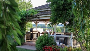 A gazebo with a barbecue setup, surrounded by greenery and a white fence. - Updated and renovated Hideaway Apartment with new kitchen! Charming! (Gordonville)