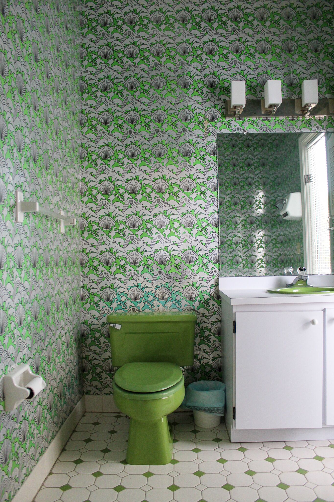 Une salle de bain avec des toilettes vertes, un lavabo blanc et un papier peint à motifs.