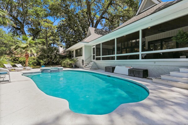 A swimming pool with a curved edge, surrounded by lounge chairs and a staircase leading to a covered area.