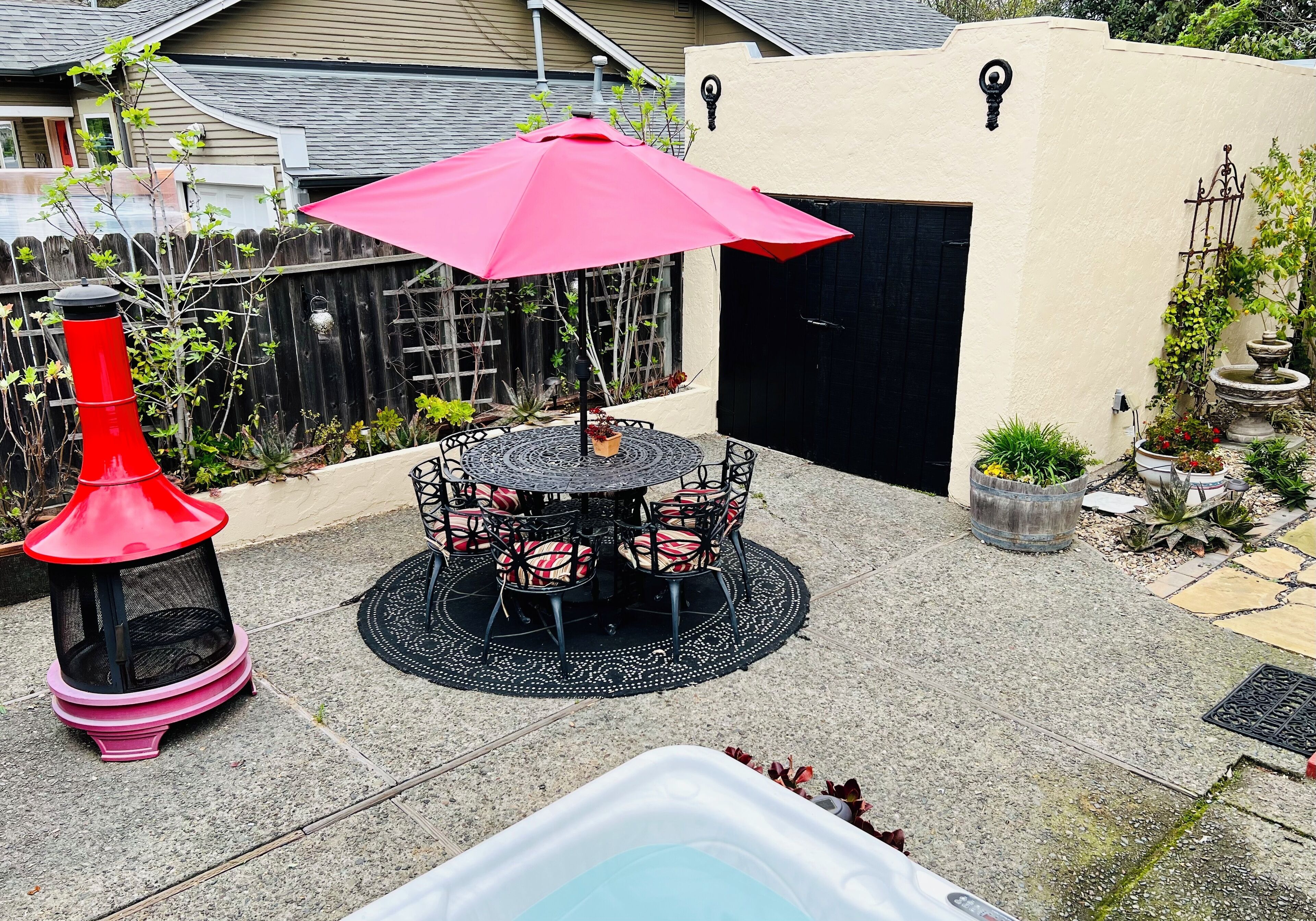 En uteplats med ett runt bord och stolar, en röd lykta och en liten pool.