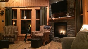 Ein gemütliches Wohnzimmer mit Holzwänden, einem Steinkamin und einem flachbildfernseher, der darüber angebracht ist.
