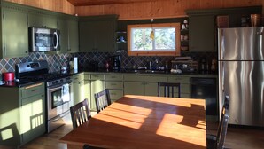 Eine Küche mit Holzausbau, einem Edelstahl-Kühlschrank, einer Mikrowelle, einem Herd und einem Esstisch mit Stühlen.