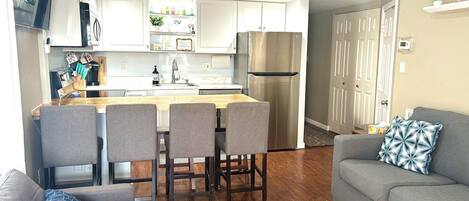 A modern kitchen with white cabinets, a stainless steel refrigerator, and a dining area with a wooden table and four chairs.