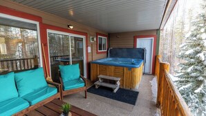 Een overdekt terras met een hottub, houten meubels en uitzicht op met sneeuw bedekte bomen.