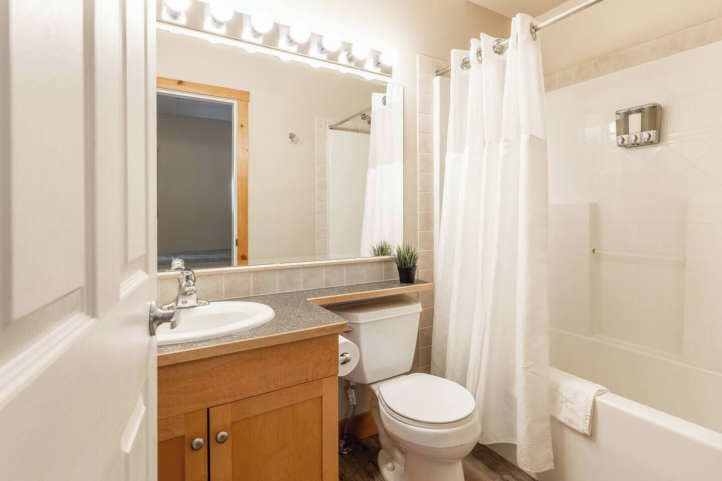 Baño con lavamanos, espejo, inodoro y zona de ducha.