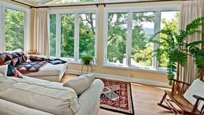 A sunroom with large windows, a sofa, a rocking chair, and a potted plant.