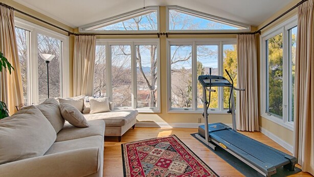 A sunroom with a large window, a treadmill, and a beige sofa.