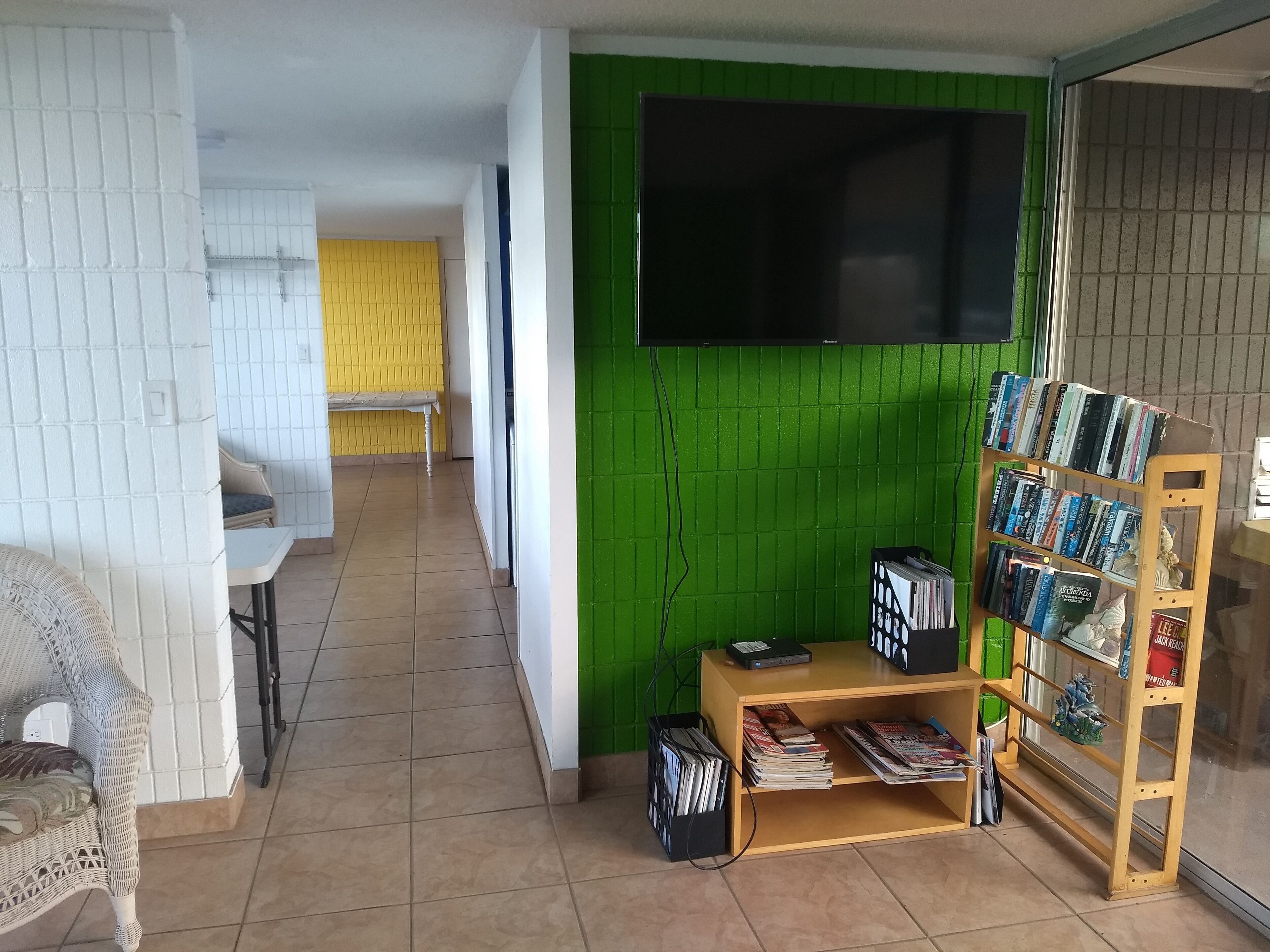 A room with a green wall, a wooden bookshelf, and a TV mounted on the wall.