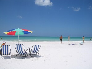 A beach with white sand, a colorful umbrella, and striped beach chairs. - CRESCENT ROYALE, SIESTA KEY BEACH, BEST BEACH LOCATION, GREAT POOL, GROUND FLOOR (Siesta Key)