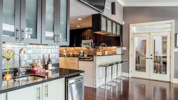 A modern kitchen with dark cabinets, a stainless steel dishwasher, a microwave, and a large TV mounted above the counter.