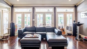 Ein geräumiges Wohnzimmer mit Ecksofa, Couchtisch, einer Deckenleuchte und großen Fenstern.