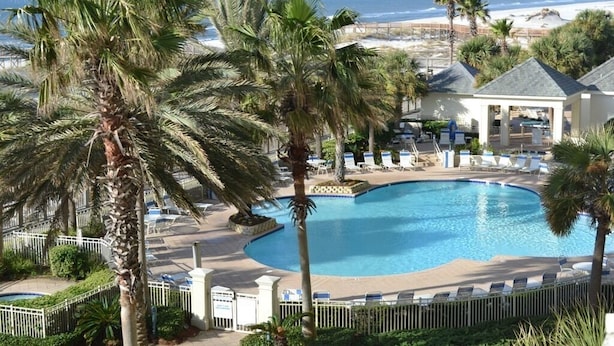 Ein Poolbereich mit Liegestühlen, Palmen und Blick auf den Strand.