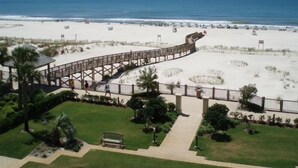 Ein Strand mit einer hölzernen Prominade, die zum Ufer führt, umgeben von Dünen und Palmen.