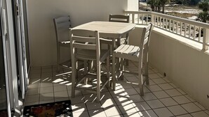 Ein Balkon mit Tisch und Stühlen, einer Fußmatte und Blick auf Strand und Meer.