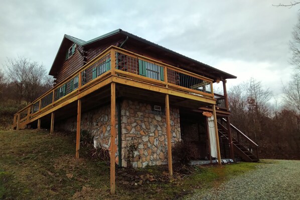 A two-story log cabin with a stone foundation, wooden deck, and a balcony.