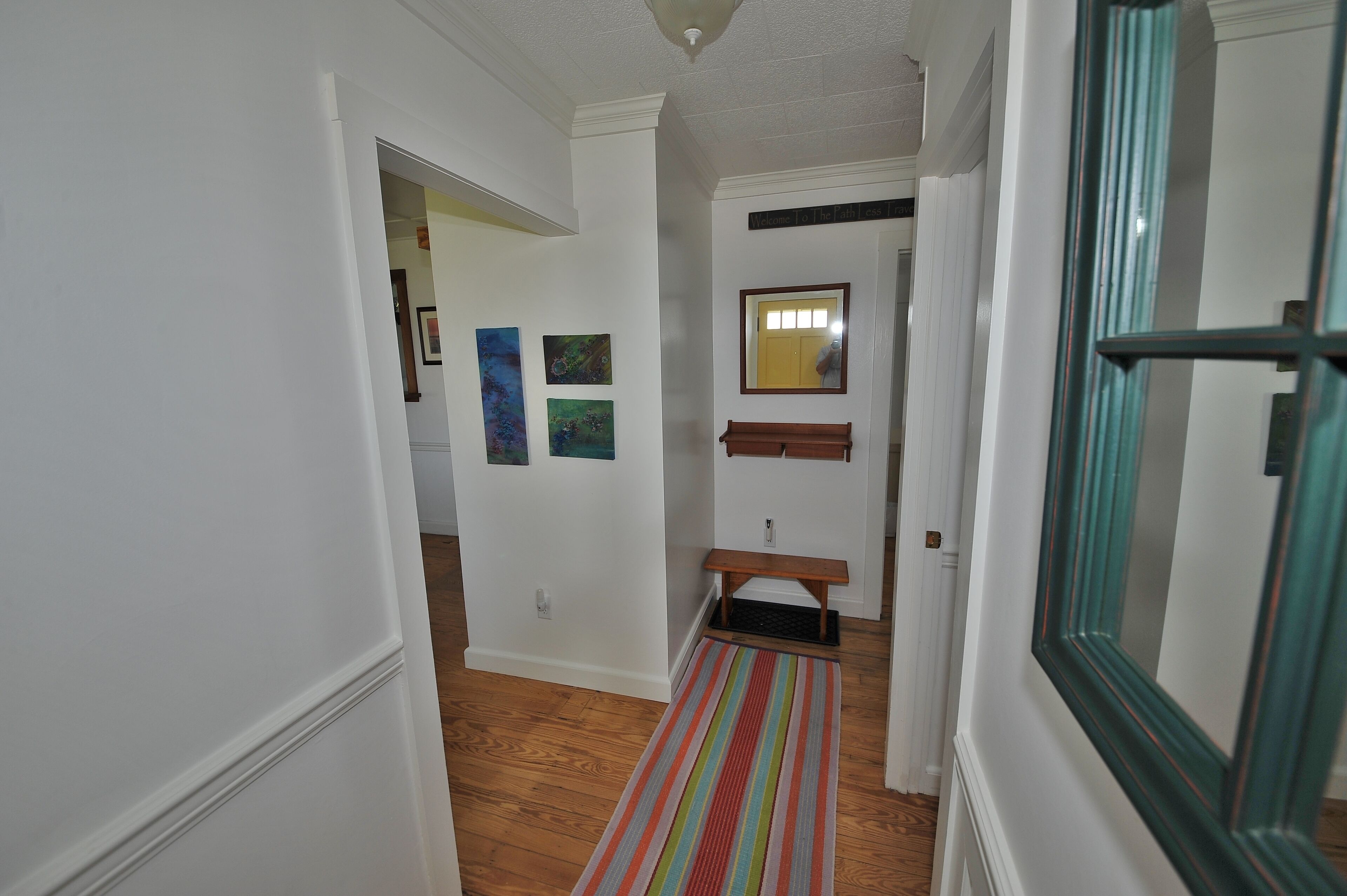 A hallway with white walls, wooden flooring, a bench, and a striped rug.