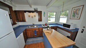 A kitchen with wooden cabinets, a blue countertop, a wooden island, a sink, a stove, a microwave, and a window with a view.